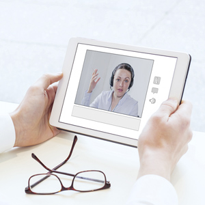 Man looking at the screen of a tablet where there is a woman wearing a headseat.