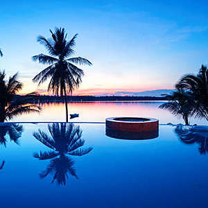 Palm trees reflecting in a luxury swimming pool with sunset views of the sea.
