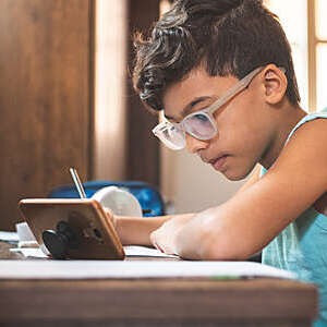 Side view of young boy using a tablet while doing his homework.