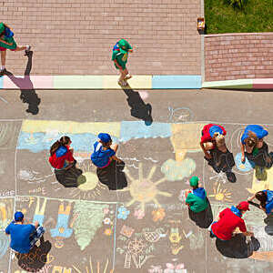  Overhead view of kids coloring a picture with colored chalk in driveway.  