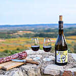 A bottle of red wine, two glasses and a salami are set on a stone wall for an aperitif overlooking the countryside.