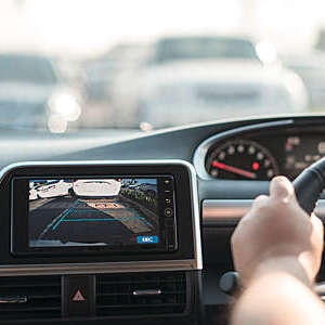 Close-up of rear-area video camera on car dashboard, with view of driver’s hand on steering wheel.