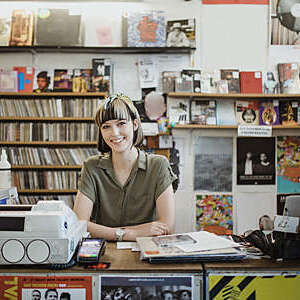 Portrait of a female retail worker standing behind the counter in a record store, smiling at camera.